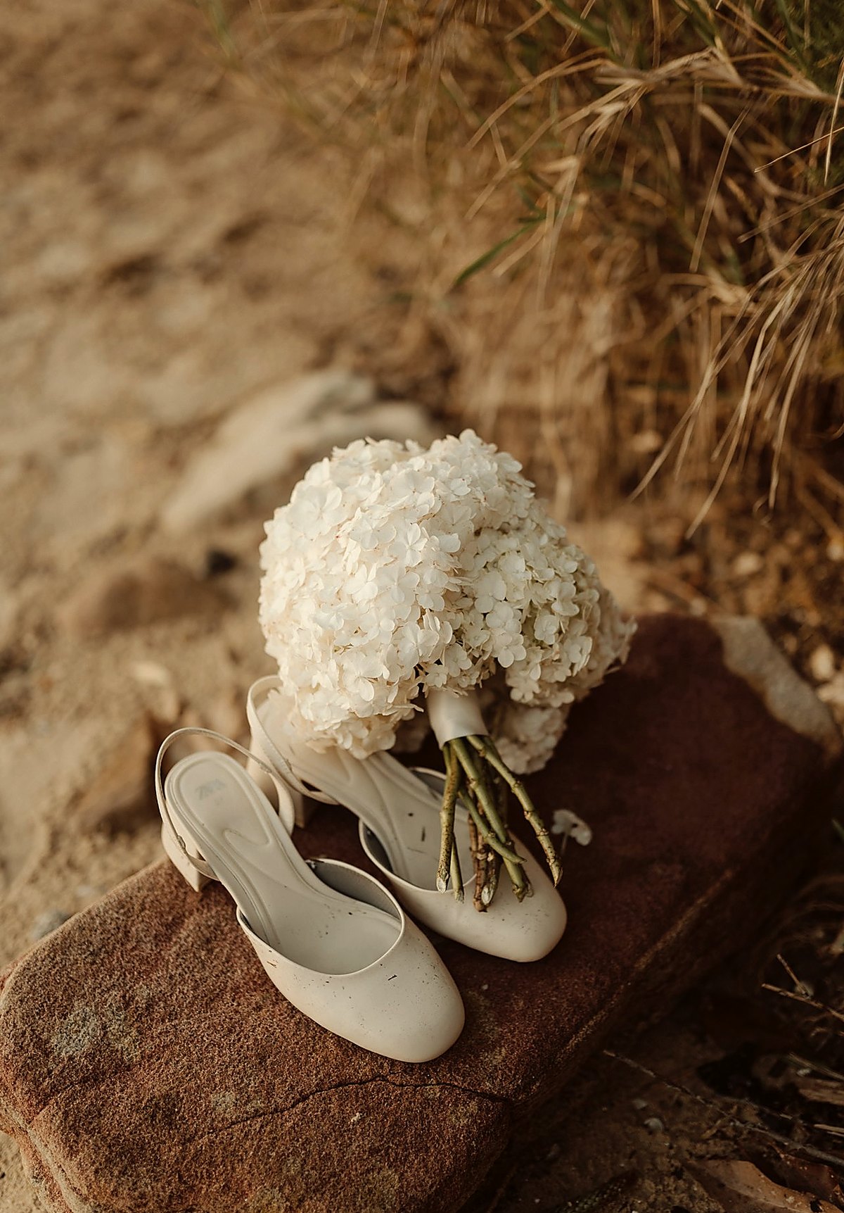 White hydrangea bouquet with bridal shoes on sandstone